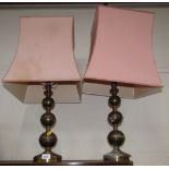 A pair of brass bulbous columned table lamps, with pink shades.