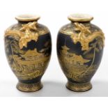 A pair of Meiji period Japanese black Satsuma vases, moulded with dragons, and decorated with a land