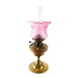 An early 20thC brass oil lamp, with clear glass funnel, brass reservoir and floral pink glass shade