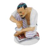 A 1920s Lomonosov Russian figure of a gentleman, crouched with bowl of rice, on a carpet,