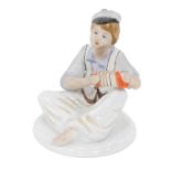 A Ukrainian Polonne porcelain figure of a child playing squeeze box, orange mark beneath, 13cm high.