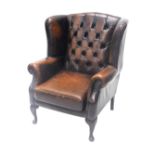 A brown leather wingback chair, with button upholstered, on cabriole legs, with pad feet.