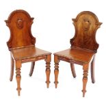 A pair of Victorian mahogany hall chairs, the shaped back with a carved shield, above a serpentine s