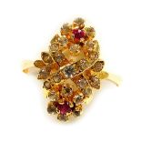 A ruby and white sapphire ring, in a double flower head and cross design, in a yellow metal high cla