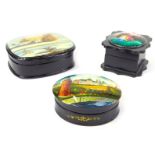 Three Russian black lacquered trinket boxes, each with a painted panel depicting various scenes,