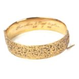 A rolled gold half hinged bangle, of floral scroll design with internal inscription From Mum and Dad