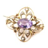 An Edwardian amethyst brooch, the oval stone in a pierced floral surround, set with seed pearls, wit