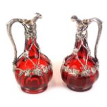 A pair of late 19th/early 20thC ruby tinted glass claret jugs, each with silver plated mounts, cast