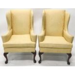 A pair of mahogany wingback armchairs in George I style, each upholstered in gold damask fabric, on