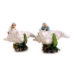 A pair of late 19thC Continental porcelain figures, modelled as a man and woman sitting within a con