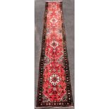 A Hamadan red ground runner, decorated with four medallions interspersed with flowers and scrolling