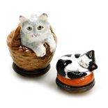 Two Halcyon Days porcelain and enamel bonbonnieres, modelled as a cat sat in a basket, 5cm high, and