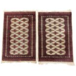 A pair of Bokhara red and cream ground prayer rugs, decorated with repeating central medallions, wit