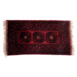 An Afghan red ground rug, with three central medallions, within repeating geometric and foliate bord