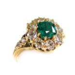 An emerald and diamond ring, the cushion shaped emerald in a surround of eight brilliant cut diamond