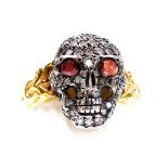 A diamond skull or memento mori ring, with ruby set eyes, in white and yellow metal, size O, 3.8g.