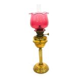 A late 19th/early 20thC brass oil lamp, with a cranberry glass shade, brass central reservoir, a Cor