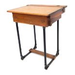 A mid 20thC oak school desk, the hinged lid enclosing a vacant interior, on two metal U shaped suppo