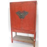 A Chinese red lacquered cabinet, the two doors with engraved brass butterfly shaped mount and stirru