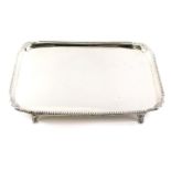 A George III silver rectangular tray, with a gadrooned border and leaf cast corners on tapering feet