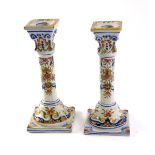 A pair of late 19thC French faience candlesticks, each on square tapering base, polychrome decorated