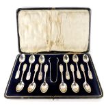 A cased set of twelve George V silver teaspoons, with claw tongs, the teaspoons of shield outer band