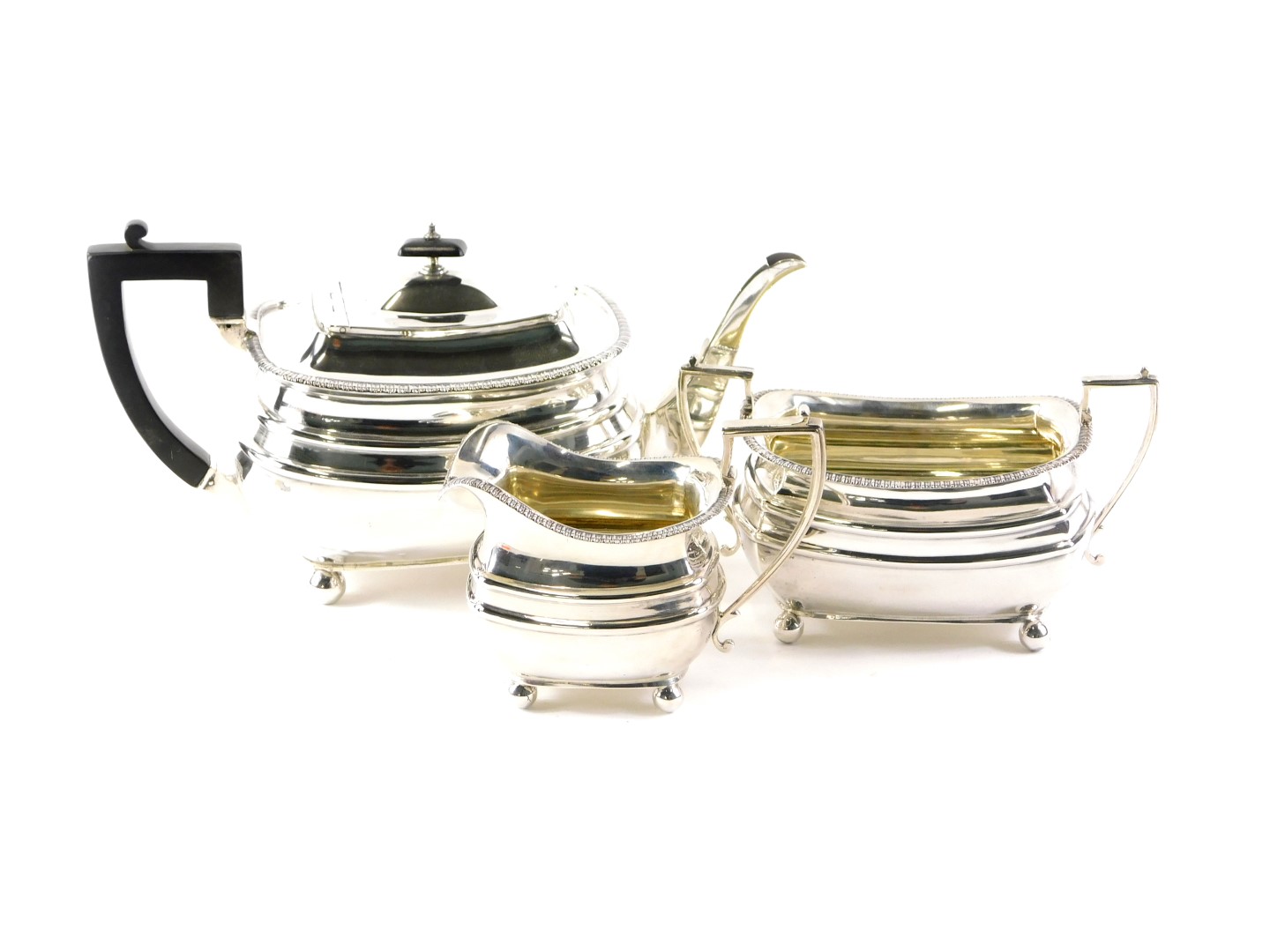 A George V silver three piece tea set, with gadrooned borders, the teapot with ebonised handle and k