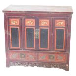A Chinese red stained side cabinet, with two panelled doors, each inset with red and gilt lacquered