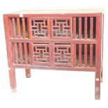 A Chinese red painted side cabinet, with two pairs of sliding fret work doors, flanked by slatted si
