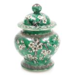 A Quing dynasty porcelain vase and cover, of baluster form, decorated with prunus blossom on a green