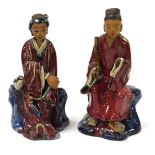 A pair of Chinese red glazed and buff stoneware figures, of a seated gentleman, and lady, the gentle