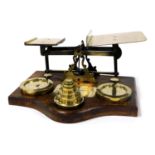 A set of early 20thC brass postage scales, raised on an oak base, with weights, from ½oz-4lbs, 38cm