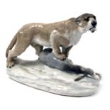 An Amphora porcelain figure of a lioness, modelled on a rocky base, with its front right paw upon a