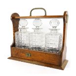 A 20thC oak cased Tantalus, containing three moulded glass square faceted spirit decanters, the Tant