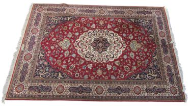 A Kashan red ground rug, decorated with a central cream and blue medallion, with flowers and foliate