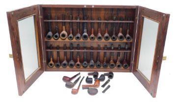 A large collection of briar and other wooden pipes, contained within a rosewood wall cabinet, stampe