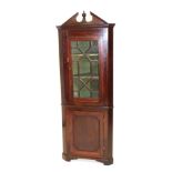 A mahogany standing corner cabinet, with a broken pediment above a single glazed door, the base with