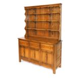 An Ercol elm dresser, with a three shelf waterfall plate rack, over three drawers above panelled cup