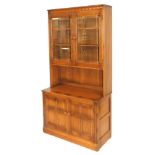 An Ercol elm cupboard display cabinet, with a carved frieze above a pair of glazed doors enclosing t
