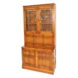 An Ercol elm cupboard display cabinet, with a carved frieze over a pair of glass doors enclosing thr