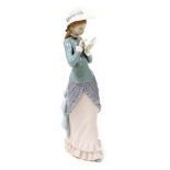 A Lladro porcelain figure of a young lady, modelled standing, wearing a bonnet and reading a book, p