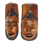 A pair of African hardwood and resin inlaid wall masks, each depicting a male face, surmounted by an