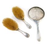 A George V silver backed dressing table set, comprising hand mirror, and two hairbrushes, each brigh
