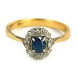 A sapphire and diamond cluster ring, the central oval sapphire in four claw setting surrounded by il