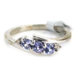 A silver dress ring, of two twist design set with three tanzanite stones with tiny diamond set ends,