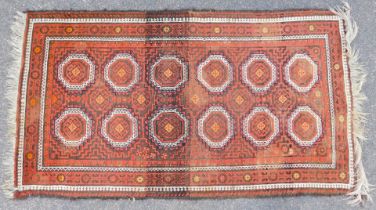 An Eastern rug, on a red ground with four medallions, orange and cream border with tassel ends, 187c