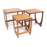 A nest of three G-Plan teak tables, each with a tiled top, raised on U shaped supports, largest 49cm