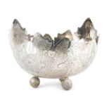 A Burmese white metal bowl, with shaped edge, the bowl decorated with leaves, flowers, etc., on thre