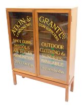 A teak two door display cabinet, with applied advertising for Atkin and Vrant Ltd Clothing and Gun s