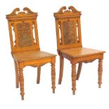 A pair of Edwardian oak hall chairs, each with a swan neck rail and carved back, 91cm high.